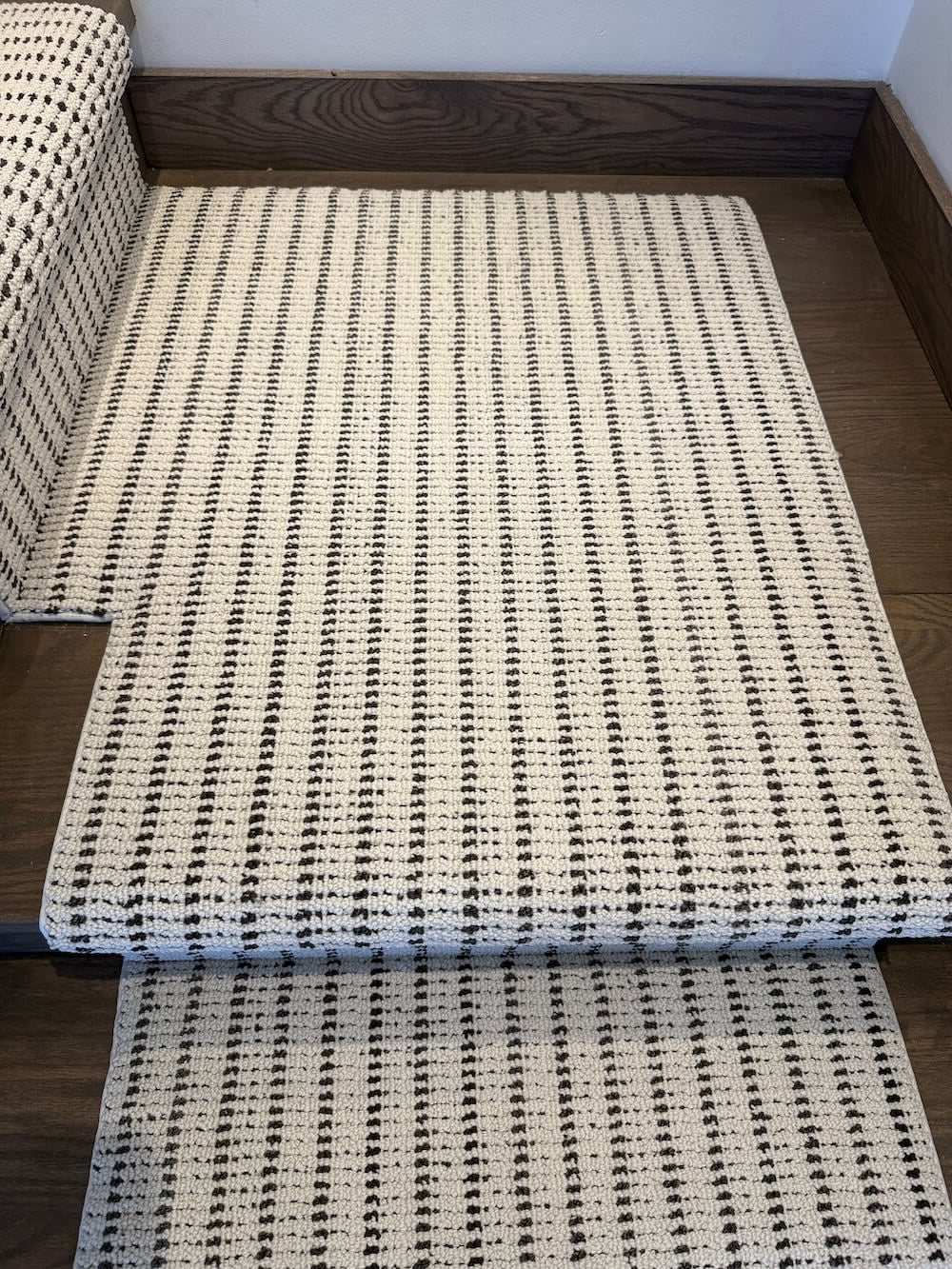 A woven area rug with a black and off-white vertical stripe pattern, shown partially rolled up on a dark wood floor next to a matching rolled section.