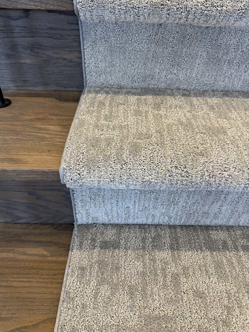 Close-up of Mallard Manor Mist Gray stair runner carpet on dark stained stairs