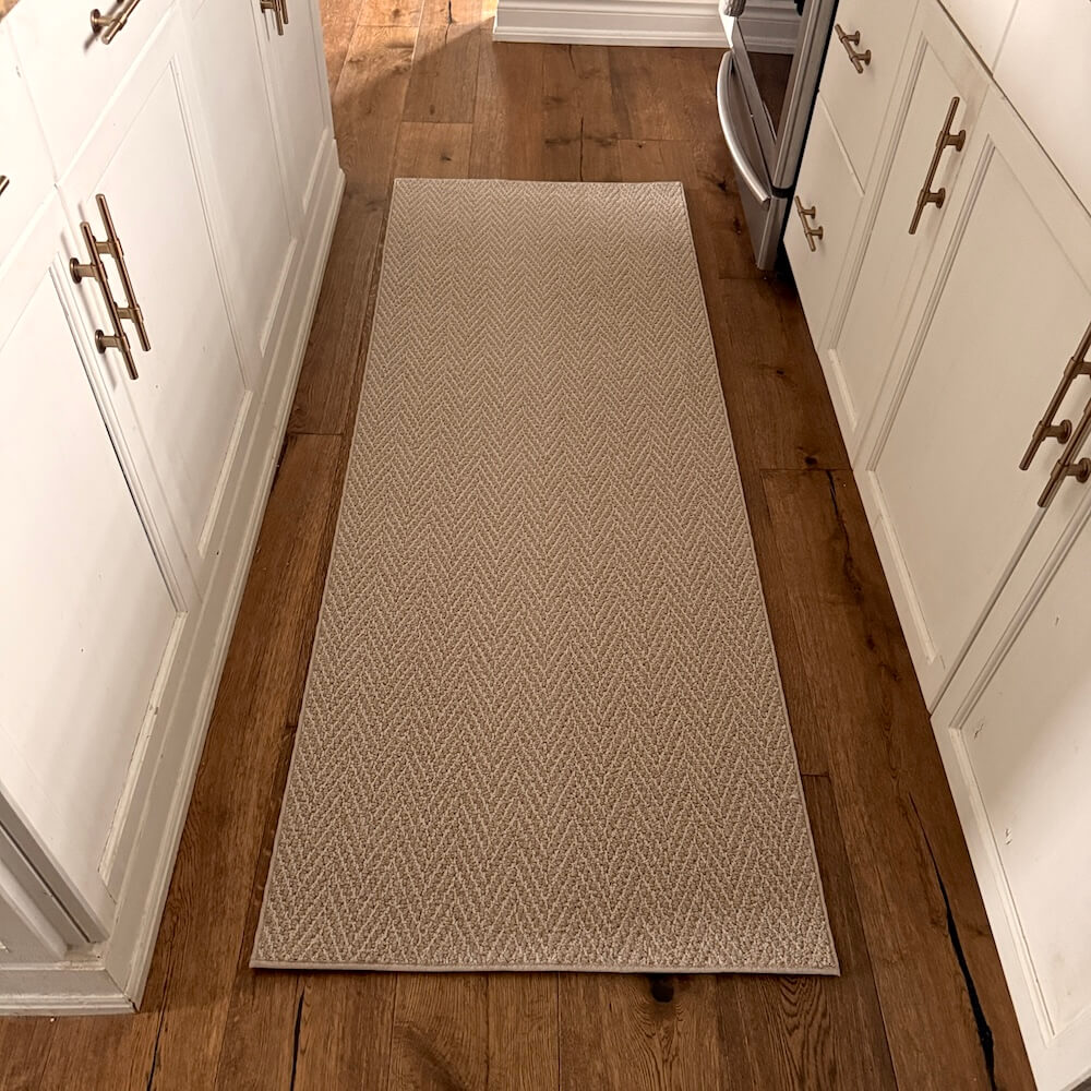 Beige patterned rug on a wooden floor between white cabinets.