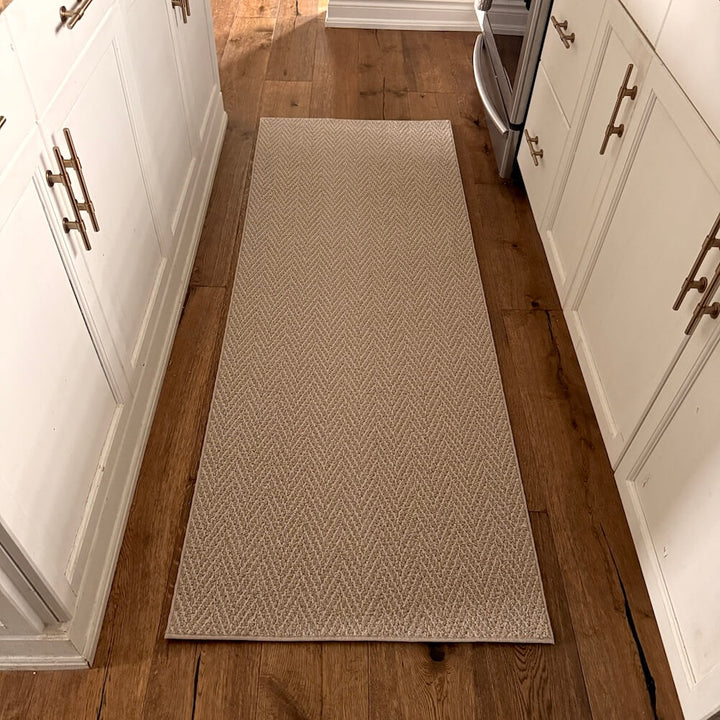Beige patterned rug on a wooden floor between white cabinets.