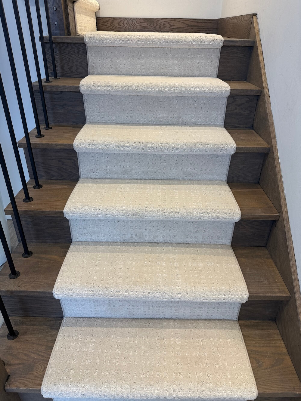 A set of indoor staircase steps covered with light beige textured carpet, set against dark wood risers and a black metal railing.