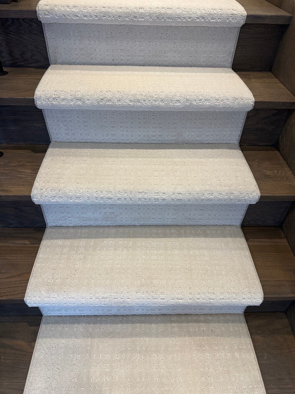 A set of carpeted stair risers in a light beige textured fabric, shown installed on a wooden staircase.