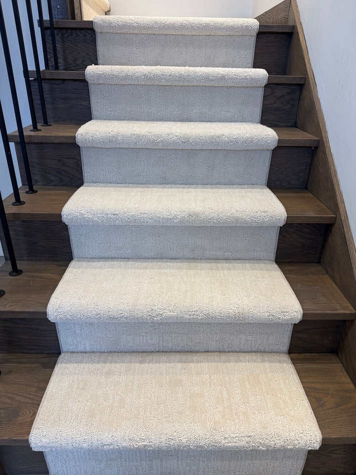 A set of indoor stairs with dark wood treads and risers, covered with light beige textured carpet steps.