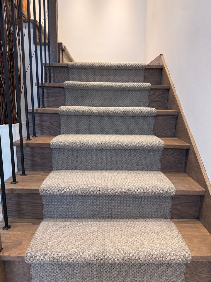 Staircase with patterned gray carpet on wooden steps in a well-lit room.
