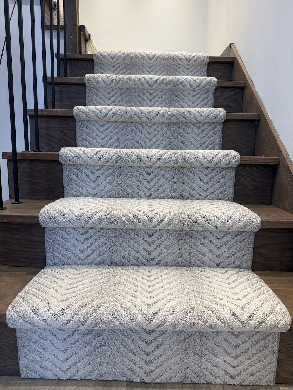 A set of carpeted stair risers with a textured chevron pattern, installed on a wooden staircase indoors.