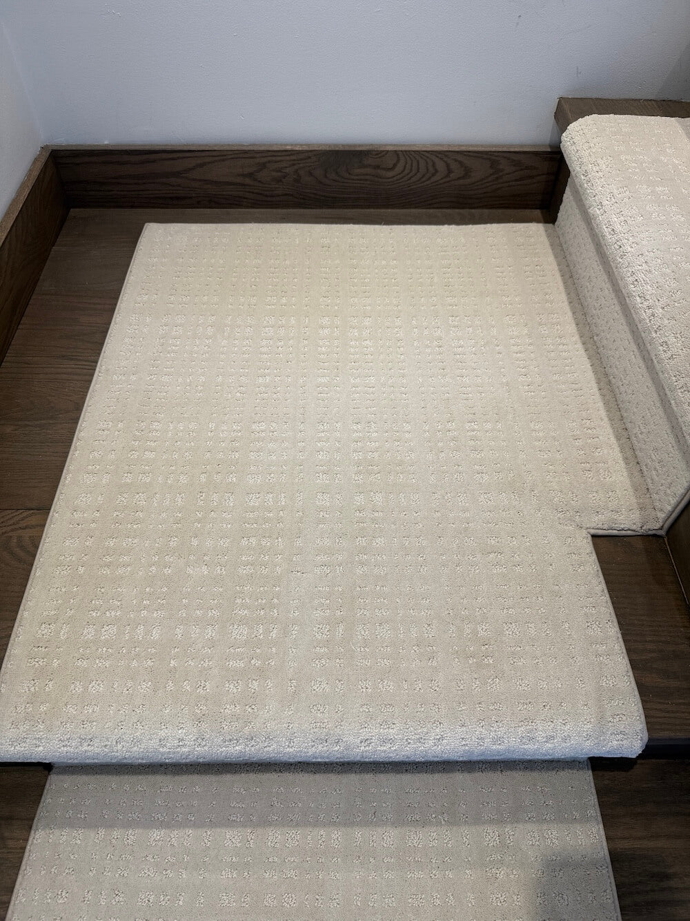 A light beige textured stair carpet pad shown installed on a wooden staircase, with a matching stair rail visible on the right side.