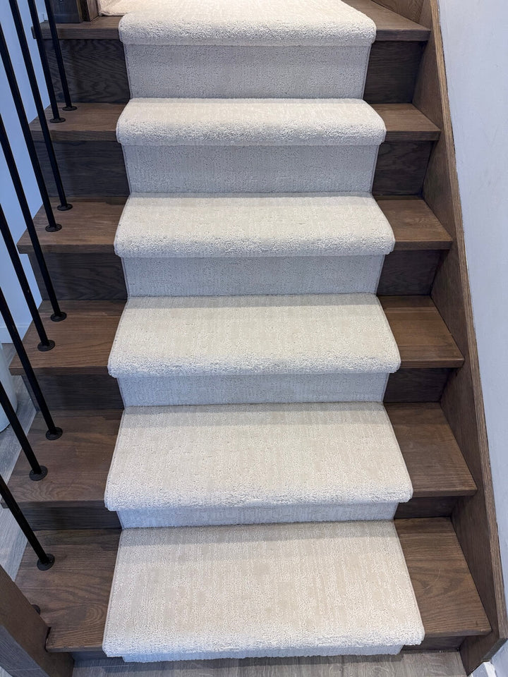 A set of indoor stairs with medium brown wooden treads and carpeted steps in a light beige or off-white textured fabric.