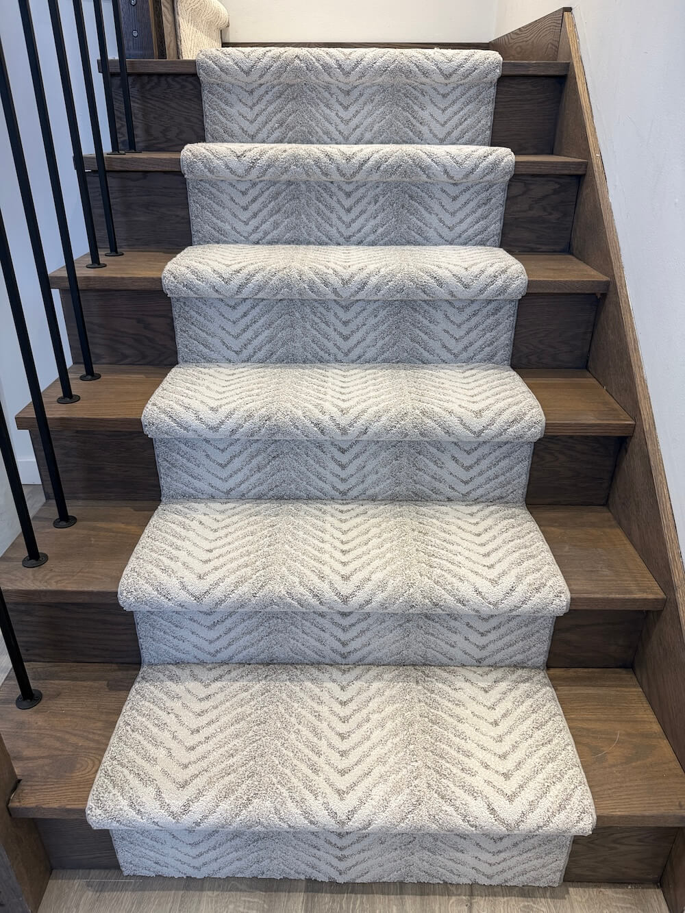 A set of five carpeted stair risers with a textured chevron pattern in light gray and white, installed on a wooden staircase.