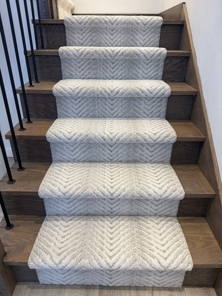 A set of five carpeted stair risers with a textured chevron pattern in light gray and white, installed on a wooden staircase.