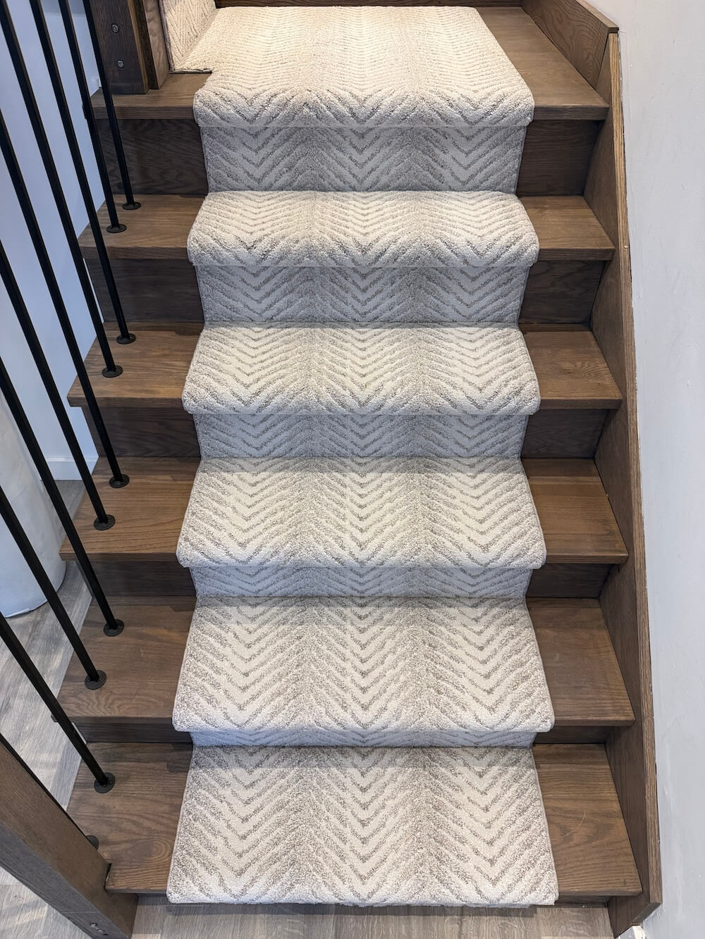 A set of light beige carpet stair runners with a textured chevron pattern, installed on a wooden staircase.