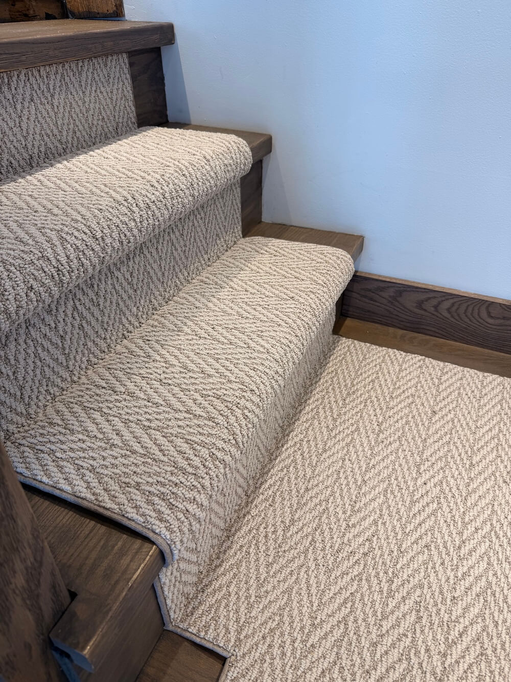 Staircase with carpeted steps and wooden handrails against a light blue wall.