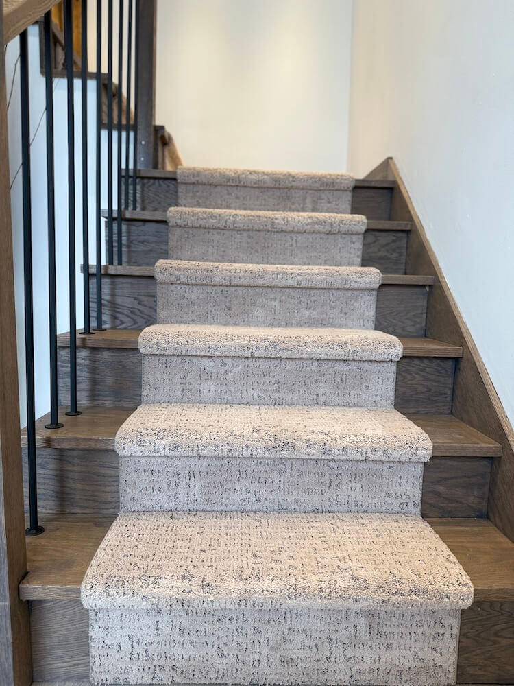 Staircase with gray carpeted steps and wooden risers in a well-lit interior setting.