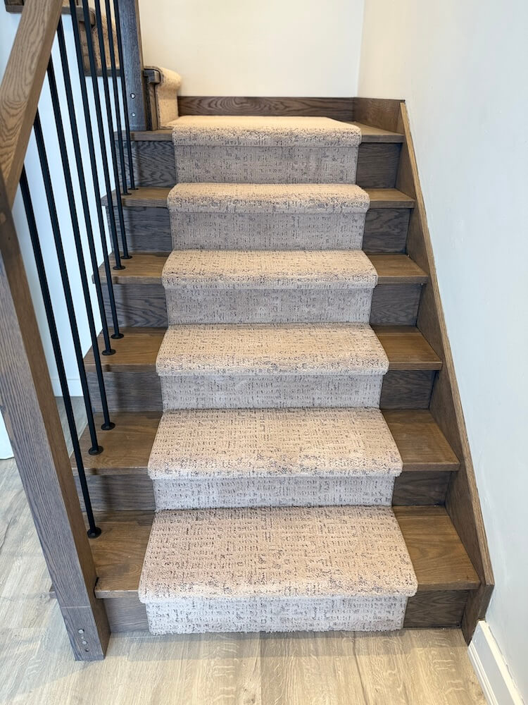 Wooden staircase with carpeted steps and black metal railing.