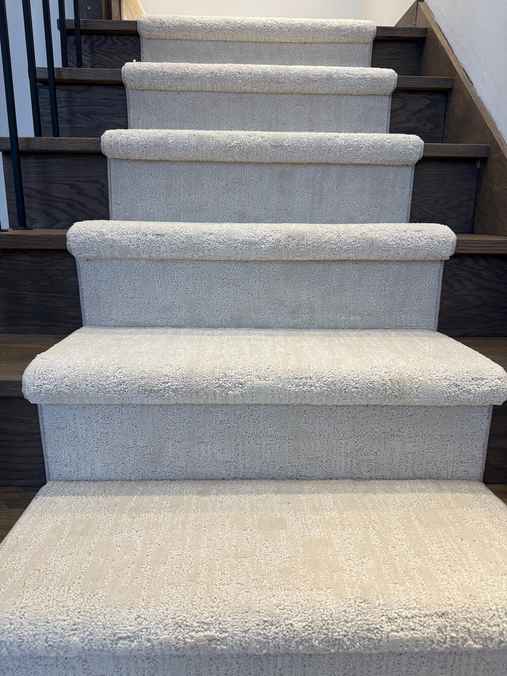 A set of carpeted stairs with light beige textured carpeting and dark wood risers and handrails.
