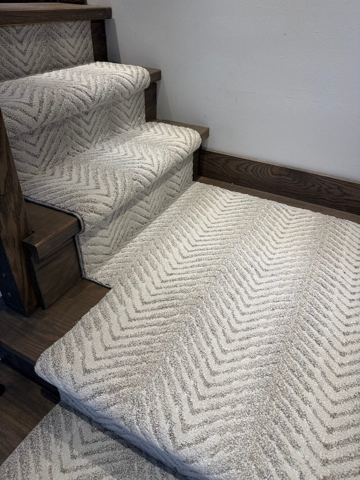 A textured stair carpet with a beige and white chevron pattern installed on wooden stairs, with a matching rectangular floor rug in front.
