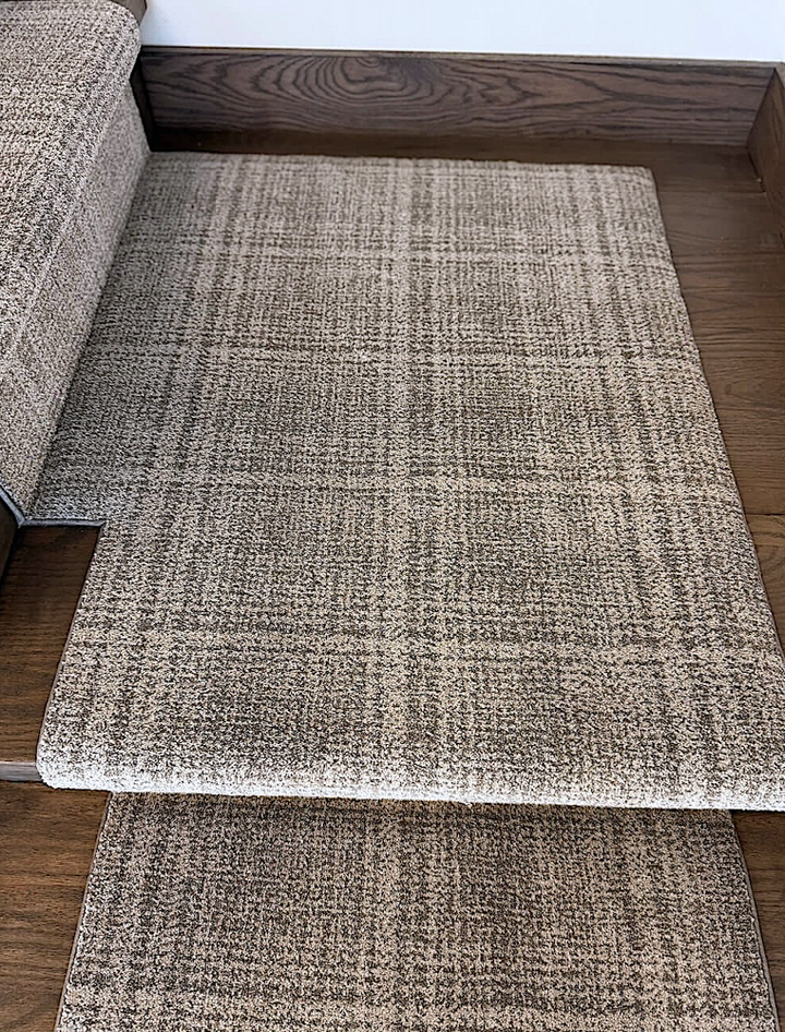Textured gray rug on a wooden floor with a wooden staircase in the background